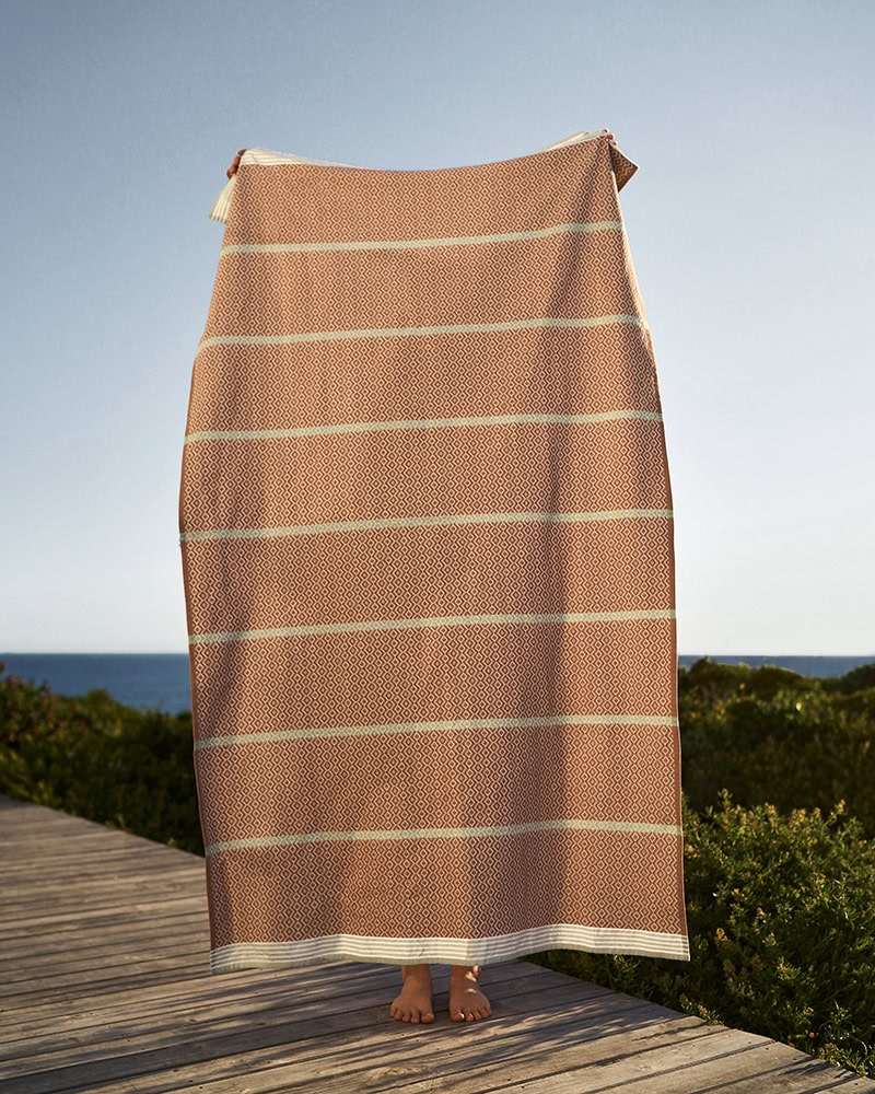 Model holding up the Fired Clay Itawuli. 100% cotton flat weave towels woven in South Africa and made for the US
