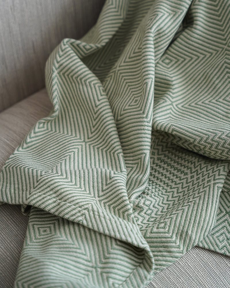 Mungo Whalebone throw blanket on a couch. Pictured in Palm.