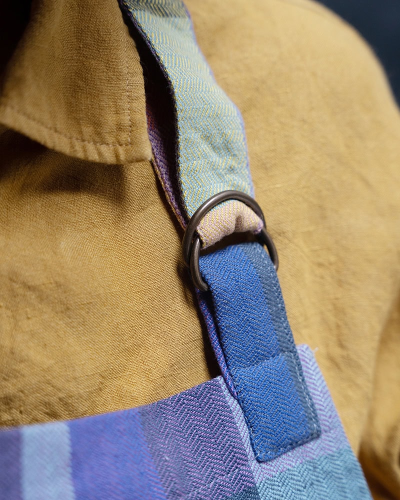 Close up view of the Mungo Alles Apron in Iris, showcasing its adjustable neck strap with d-ring.